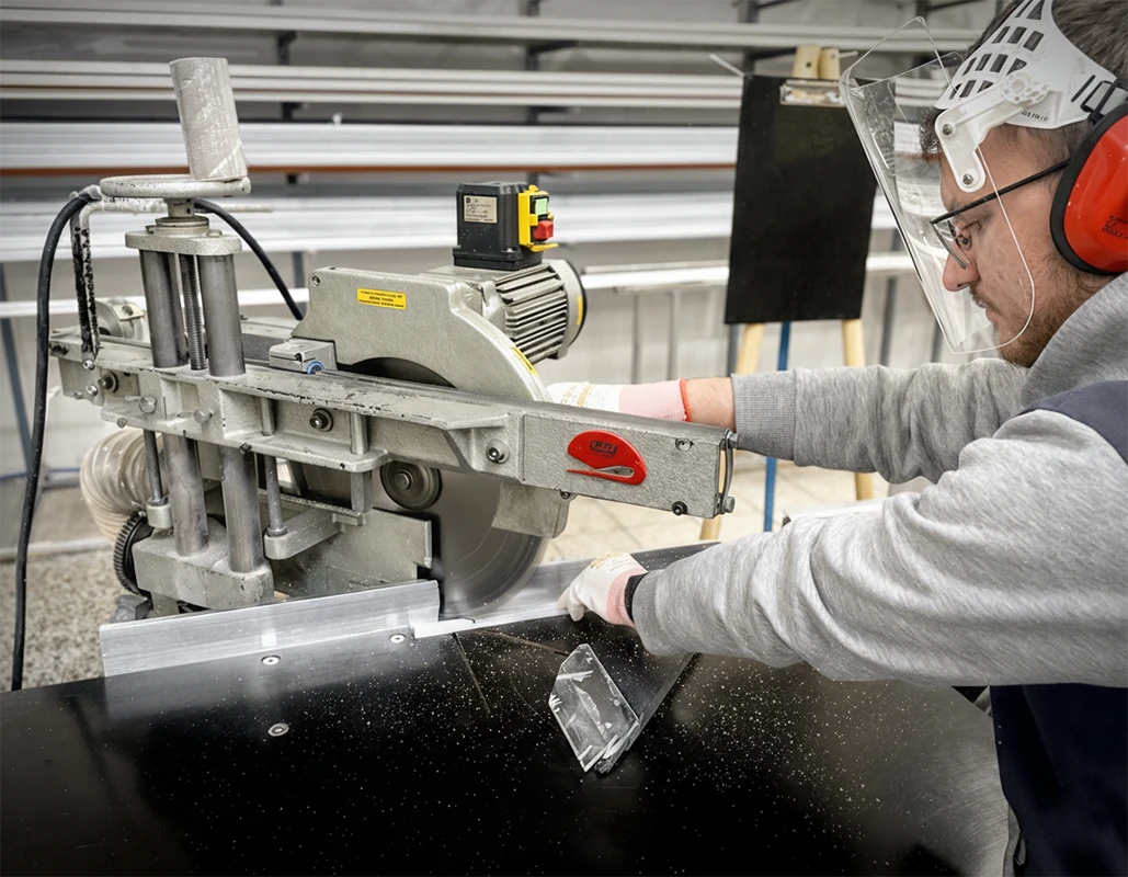 Lucrător care taie materialul pentru fabricarea plaselor anti-insecte, alături de prezentarea tipurilor de plasă – gri, neagră și PET rezistentă